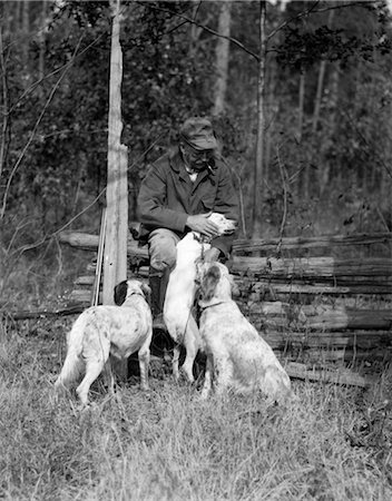 simsearch:846-02792988,k - 1920ER JAHRE ÄLTERER MANN SITZT MIT GEWEHR GEGEN ZAUN STREICHELN EINES DER DREI JAGDHUNDE RUHEN Stockbilder - Lizenzpflichtiges, Bildnummer: 846-02792988