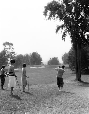 1920s 1930s MALE GOLFER DRIVING DOWN FAIRWAY TWO WOMEN AND CADDY LOOK ON AT THE BERKSHIRE HOTEL & COUNTRY CLUB MA Foto de stock - Con derechos protegidos, Código: 846-02793017