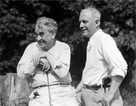 1920s 1930s 2 ELDERLY MEN HOLDING GOLF CLUBS SITTING ON A TREE STUMP LOOKING TOWARDS GOLF COURSE Stock Photo - Rights-Managed, Code: 846-02793032