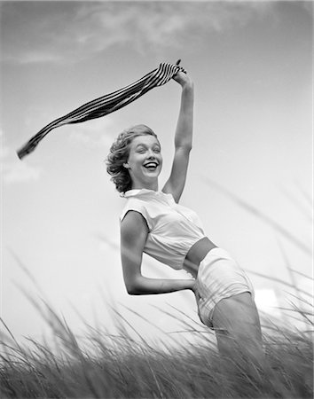 fashions 1950s - 1950s 1960s SMILING YOUNG WOMAN IN WHITE SHORTS AND BLOUSE BENDING BACK WAVING SCARF IN THE WIND STANDING ON GRASSY BEACH DUNE Stock Photo - Rights-Managed, Code: 846-02793071