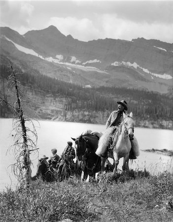 1920s 1930s TWO WOMEN ONE MAN RIDING HORSES WESTERN SADDLES COWBOY WEARING WOOL CHAPS BY MOUNTAIN LAKE IN CANADA Stock Photo - Rights-Managed, Code: 846-02793153