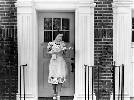 food in 1940s - 1940s WOMAN IN AN APRON STANDING OUTSIDE DOORWAY HOLDING A QUART OF MILK AND READING NEWSPAPER E Stock Photo - Rights-Managed, Code: 846-02793177