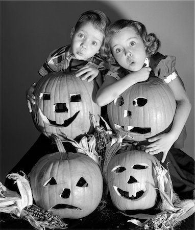 retro usa black and white - 1950s BOY AND GIRL STANDING BEHIND AND OR HOLDING FOUR JACK-O-LANTERNS WITH INDIAN CORN MAKING SPOOKY FACES Stock Photo - Rights-Managed, Code: 846-02793199