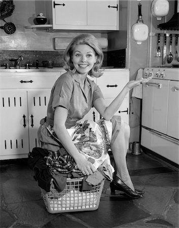 1960s SMILING HOUSEWIFE IN KITCHEN SITTING ON TOP OF FULL LAUNDRY BASKET HOLDING OUT HAND Foto de stock - Con derechos protegidos, Código: 846-02793278