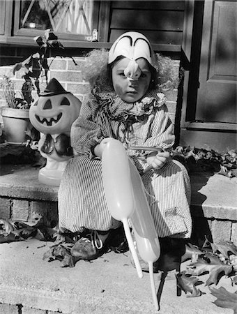 ENFANT DES ANNÉES 1970 DANS TRICK OR TREAT CLOWN COSTUME ASSIS SUR LA PORTE AVANT ÉTAPE TENANT DES BALLONS Photographie de stock - Rights-Managed, Code: 846-02793308