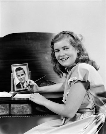 1940s SMILING GIRL AT DESK WRITING LETTER PHOTO OF BOY OR MAN IN FRAME Stock Photo - Rights-Managed, Code: 846-02793458