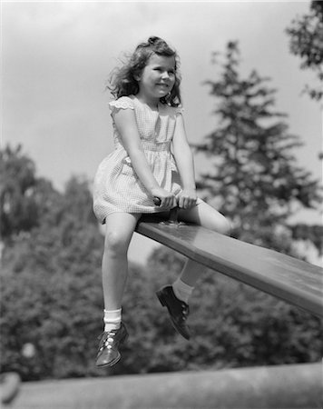 1950s 7 YEAR OLD GIRL WEARING DRESS SIT ON SEESAW TEETER TOTTER IN UP POSITION IN PARK SMILING FUN PLAYGROUND PLAY UP AND DOWN Foto de stock - Con derechos protegidos, Código: 846-02793459