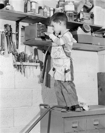 faire - 1950s 4 YEAR OLD BOY IN GARAGE TOOL SHED STANDING ON CABINET TO REACH BOX ON SHELF Foto de stock - Con derechos protegidos, Código: 846-02793461