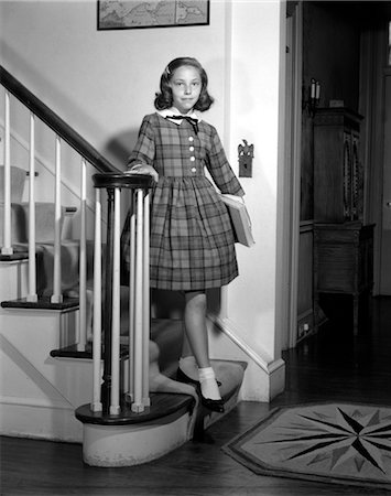 1950s TEENAGE GIRL IN PLAID DRESS AND WHITE ANKLE SOCKS STANDING ON STAIRWAY HOLDING BANISTER CARRYING SCHOOL BOOKS Stock Photo - Rights-Managed, Code: 846-02793506