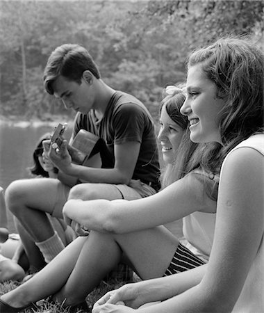 1960s SIDE VIEW OF TEEN GIRLS SEATED ON BANK LISTENING TO TEEN BOY PLAY GUITAR Stock Photo - Rights-Managed, Code: 846-02793511