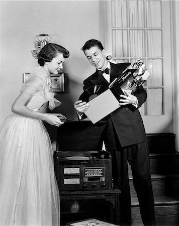 1950s TEEN COUPLE BOY AND GIRL IN PROM FORMAL WEAR PLAYING PHONOGRAPH RECORDS IN HOME LIVING ROOM Foto de stock - Con derechos protegidos, Código: 846-02793599