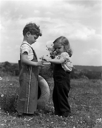 1940s 1950s LITTLE GIRL HANDING DAISIES TO BOY STANDING IN FIELD OF FLOWERS Foto de stock - Con derechos protegidos, Código: 846-02793689