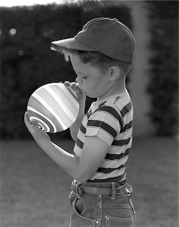 1950s PROFILE OF BOY IN BASEBALL CAP & STRIPED T-SHIRT BLOWING UP STRIPED BALLOON Foto de stock - Con derechos protegidos, Código: 846-02793703