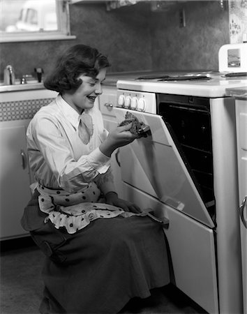 retro picture of lady cooking - 1950s YOUNG WOMAN GIRL WEARING APRON KNEELING OPENING OVEN DOOR KITCHEN STOVE COOKING Stock Photo - Rights-Managed, Code: 846-02793793