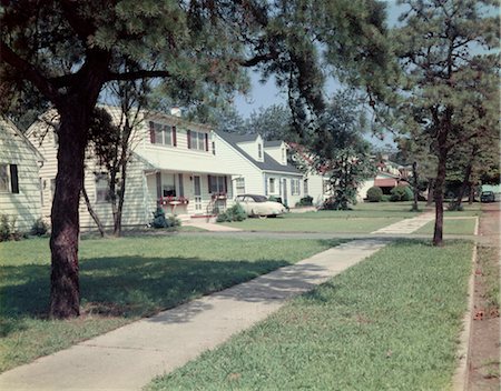 simsearch:846-03163542,k - 1950s SUBURBAN STREET WHITE HOUSES WITH SIDEWALK RUNNING DOWN MIDDLE OF IMAGE YARD GREEN GRASS SPRING LAKE NJ Foto de stock - Direito Controlado, Número: 846-02793935