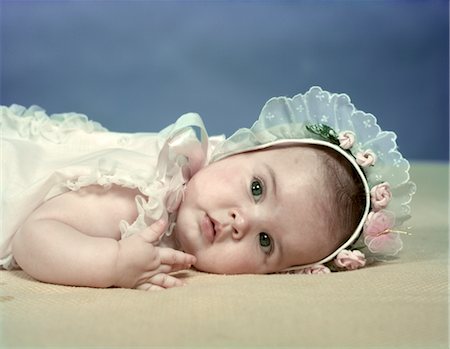 1950s BABY GIRL LYING ON BEIGE BLANKET WEARING BABY BONNET WITH LACE AND PINK ROSEBUD TRIM SPRING SEASON Stock Photo - Rights-Managed, Code: 846-02793943