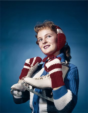 ANNÉES 1960 FEMME SOURIANTE PORTANT DES MITAINES ROUGES OREILLE CACHE-OREILLES ET BLEU PULL TENANT DES PATINS À GLACE, LEVANT LES CHEVEUX STUDIO HIVER ROUGE Photographie de stock - Rights-Managed, Code: 846-03164517