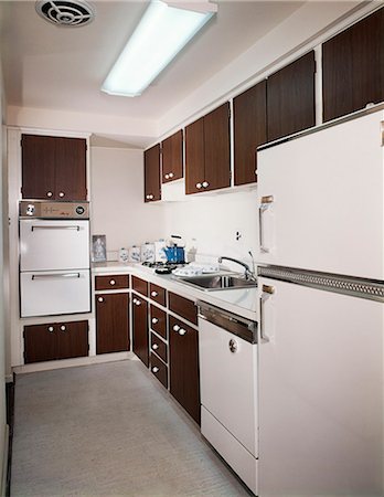 1970s NARROW GALLEY STYLE KITCHEN WITH DARK WOODEN CABINETS AND WHITE APPLIANCES Stock Photo - Rights-Managed, Code: 846-03164687