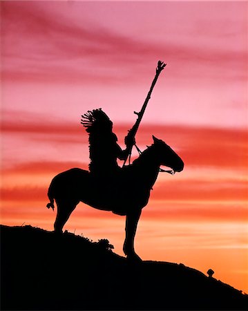 1970s SUNSET SILHOUETTE OF NATIVE AMERICAN MAN WEARING HEADDRESS ON HORSE AT TOP OF A HILL Foto de stock - Con derechos protegidos, Código: 846-03164696