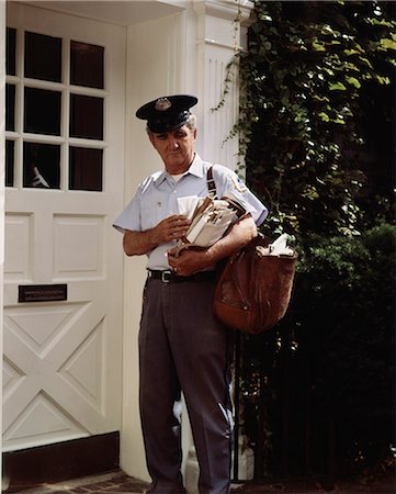 simsearch:846-03165166,k - 1970s MIDDLE AGED MAILMAN STANDING BY WHITE DOOR SORTING MAIL FOR DELIVERY Foto de stock - Direito Controlado, Número: 846-03165175