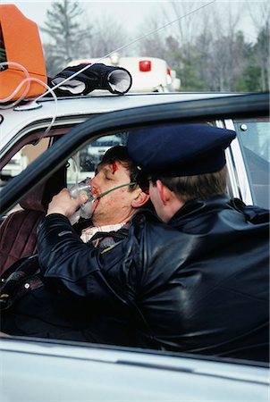 dangerous accident - 1980s POLICE OFFICER ADMINISTERING OXYGEN TO MAN AUTOMOBILE ACCIDENT VICTIM Foto de stock - Con derechos protegidos, Código: 846-03165206