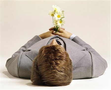 sterben - ANNÉES 1970 HOMME COUCHÉ VUE DESSUS DE TÊTE TENANT FLEURS POITRINE PUSHING UP DAISIES MORT CADAVRE Photographie de stock - Rights-Managed, Code: 846-03165834