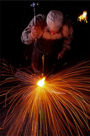 BLACKSMITH WORKING WHITE HOT IRON WITH A HAMMER RED AND ORANGE SPARKS FLYING IN ALL DIRECTIONS Stock Photo - Rights-Managed, Code: 846-03165887