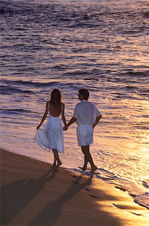 COUPLE MARCHANT LE LONG DE LA PLAGE AU COUCHER DU SOLEIL PAR LE BORD DE L'EAU Photographie de stock - Rights-Managed, Code: 846-03165894