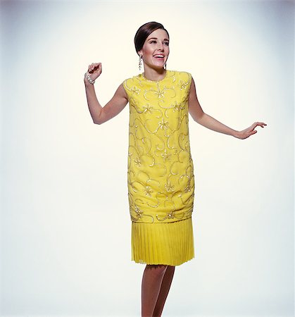 ANNÉES 1960 FEMME BRUNE SOURIANTE MODÉLISATION JAUNE PAILLETÉ VÊTEMENTS ROBE DE COCKTAIL Photographie de stock - Rights-Managed, Code: 846-03165982