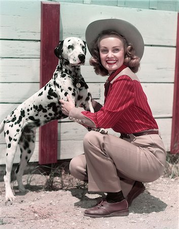 1940s 1950s SMILING WOMAN WEARING WESTERN COWGIRL OUTFIT KNEELING PETTING DALMATIAN DOG Fotografie stock - Rights-Managed, Codice: 846-03166362