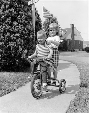 simsearch:846-05646711,k - 1960ER JAHREN ZWEI KINDER REITEN AUF DREIRAD FAHRRAD BÜRGERSTEIG Stockbilder - Lizenzpflichtiges, Bildnummer: 846-03163399