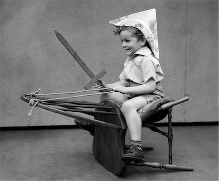 ANNÉES 1930 GARÇON JOUER ÉPÉE EN BOIS CHAISE DE CIRCONSCRIPTION CHAPEAU DE PAPIER COMME UN CHEVAL Photographie de stock - Rights-Managed, Code: 846-03163471