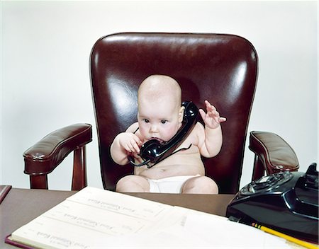 1960s CHUBBY BABY SITTING LEATHER CHAIR AT OFFICE DESK HOLDING TELEPHONE Stock Photo - Rights-Managed, Code: 846-03163791