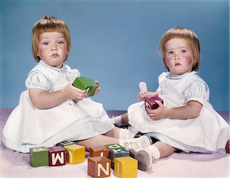 1950s 1960s PORTRAIT TWO TWIN BABY GIRLS WEARING DRESSES PLAYING WITH TOY BLOCKS Stock Photo - Rights-Managed, Code: 846-03163859