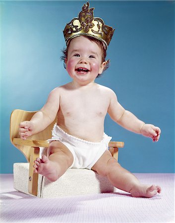 1960s SMILING HAPPY BABY WEARING CROWN SITTING ON BOOSTER SEAT CHAIR Foto de stock - Direito Controlado, Número: 846-03163925