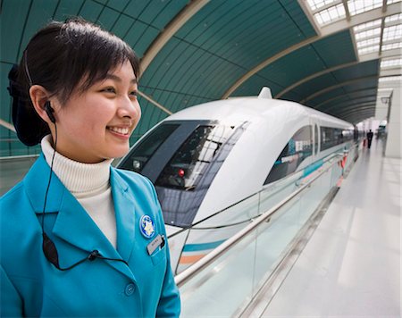 simsearch:841-03676981,k - Une hôtesse de femme souriante portant un permanent de bouchons d'oreille téléphone portable à côté d'un train à lévitation magnétique sur la plate-forme de la voie ferrée en Shanghai, Chine, Asie Photographie de stock - Rights-Managed, Code: 841-05796114
