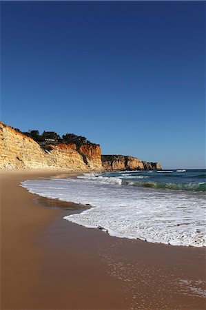 A wave breaks on golden sands flanked by steep cliffs, typical of the Atlantic coastline near Lagos, Algarve, Portugal, Europe Stock Photo - Rights-Managed, Code: 841-06032608