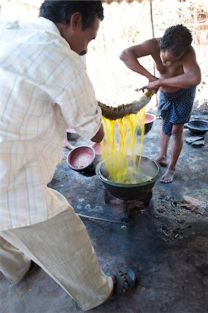 Two men squeezing yellow dye out of cotton fabric over a metal bowl heated over gas flame, Naupatana weaving village, rural Orissa, India, Asia Foto de stock - Con derechos protegidos, Código: 841-06447808