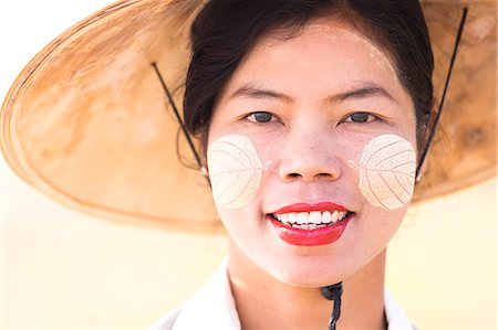 Backlit portrait of local woman wearing traditional bamboo hat and Thanaka face painting in the shape of leaves on her cheeks, near Mandalay, Myanmar (Burnma), Asia Foto de stock - Direito Controlado, Número: 841-06805735