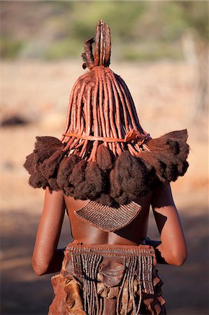 Rear view of young Himba woman showing traditional leather clothing and jewellery, hair braiding and skin covered in Otjize, a mixture of butterfat and ochre, Kunene Region (formerly Kaokoland) in the far north of Namibia Foto de stock - Direito Controlado, Número: 841-07081786