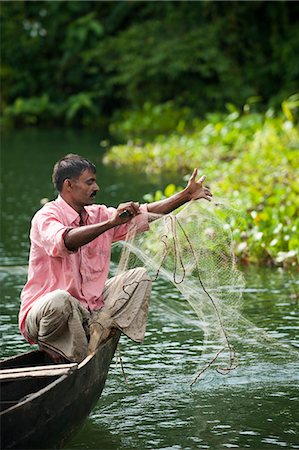 Side view fisherman is throwing fishing net to catch fish from lake in  front of rainforest in st. martin's island, Bangladesh Stock Photo