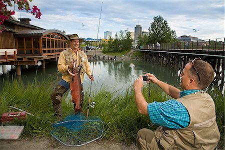 Fisherman poses with King Salmon while getting his photo taken at Ship Creek in downtown Anchorage, Alaska during Summer Foto de stock - Direito Controlado, Número: 854-03538047