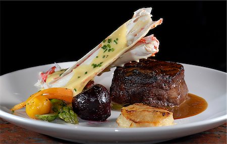 Close up of prepared dish of Snake River farm Kobe beef tenderloin truffled demi glace, Alaskan Red King Crab au gratin with lemon butter sauce and sauted baby vegetables with potato galette Foto de stock - Con derechos protegidos, Código: 854-03538365