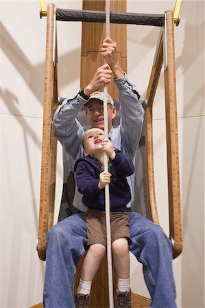 Grandfather and toddler grandson sit together and lift themselves with a rope and pulley system at the Imaginarium, Anchorage Museum at the Rasmuson Center, Southcentral Alaska, Summer Stock Photo - Rights-Managed, Code: 854-03740016