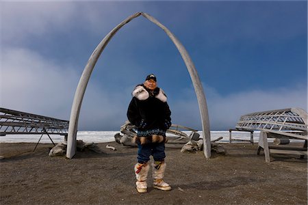 Mâle chasseur Inupiaq Eskimo portant son parka Eskimo (Atigi), le chapeau de peau de phoque et le loup de la peau de Maklak avec semelles de phoque barbu peau (Ugruk) se présenter devant une arche d'os de baleines boréales et les oumiaks, les Barrow, Alaska arctique, été Photographie de stock - Rights-Managed, Code: 854-03845455