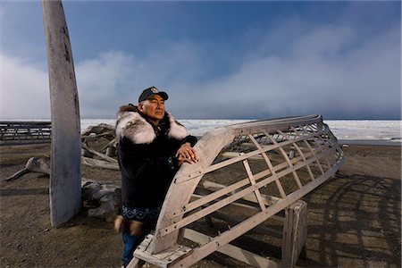 Male Inupiaq Eskimo hunter wearing his Eskimo parka (Atigi), seal skin hat and wolf skin Maklak's with soles made from bearded seal skin (Ugruk) standing in front of a Bowhead whale bone arch and Umiaqs, Barrow, Arctic Alaska, Summer Foto de stock - Direito Controlado, Número: 854-03845456