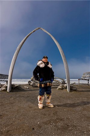 eskimo clothing - Male Inupiaq Eskimo hunter wearing his Eskimo parka (Atigi), seal skin hat and wolf skin Maklak's with soles made from bearded seal skin (Ugruk) standing in front of a Bowhead whale bone arch and Umiaqs, Barrow, Arctic Alaska, Summer Stock Photo - Rights-Managed, Code: 854-03845453