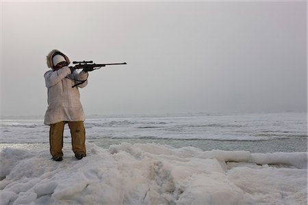 Female Inupiaq Eskimo hunter wearing a Eskimo parka(Atigi) aims a rifle towards the open water of the Chukchi Sea, Barrow, Arctic Alaska, Summer Foto de stock - Con derechos protegidos, Código: 854-03845524