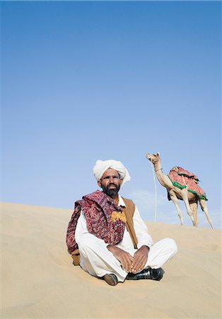 Man sitting in a desert with a camel in the background, Thar Desert, Jaisalmer, Rajasthan, India Stock Photo - Rights-Managed, Code: 857-03192651