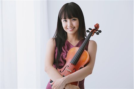 Femme asiatique vêtue d'une robe pourpre, tenant un violon et souriant à la caméra Photographie de stock - Rights-Managed, Code: 859-06404923